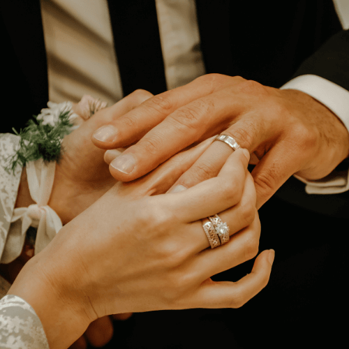 Ring Exchange: Woman placing a silver wedding band on a man's finger.