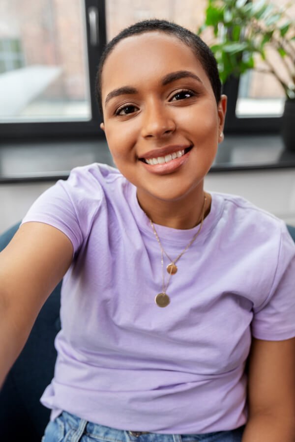 technology and people concept - happy smiling african american woman with taking selfie sitting in chair at home