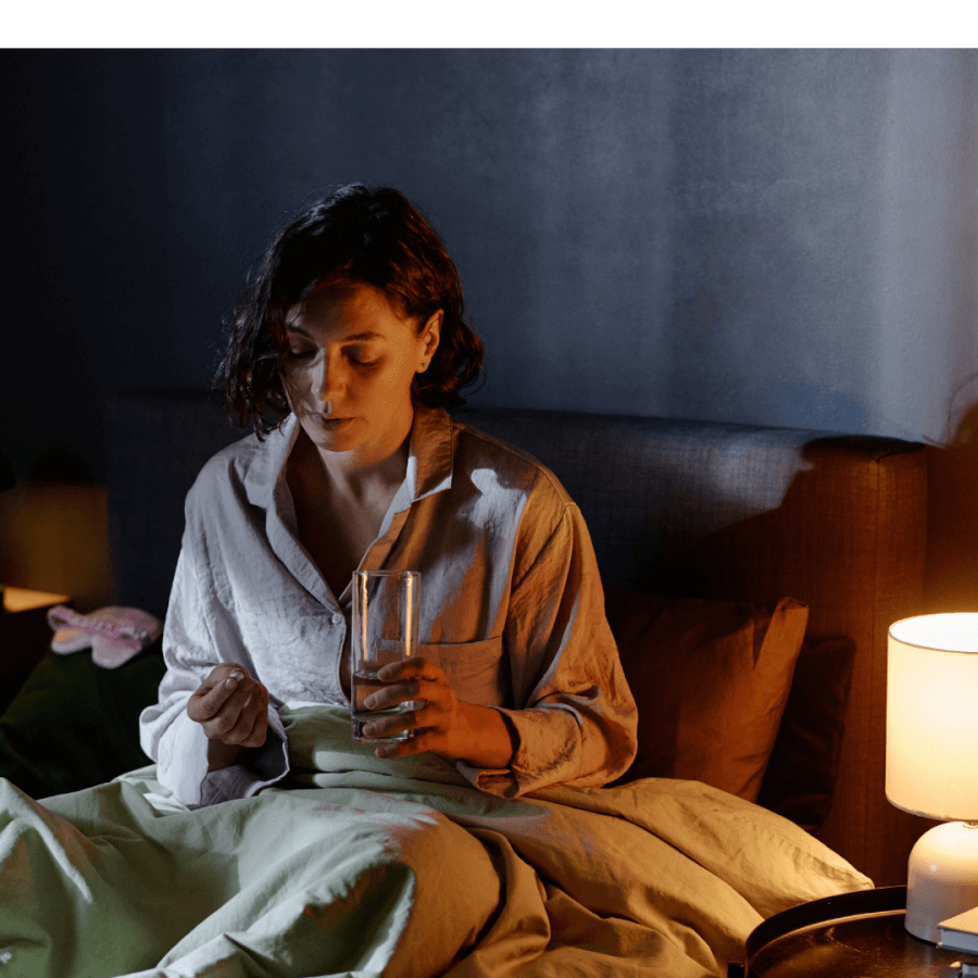 A tired woman lying awake in bed at night hold a glass of water on one hand, looking fatigued from lack of sleep, in a dimly lit bedroom. She need to improve her sleep quolity.